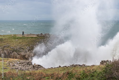 People watching the huge waves crashing on a breakwater. Weather alert on the coast with strong wind and large waves.
