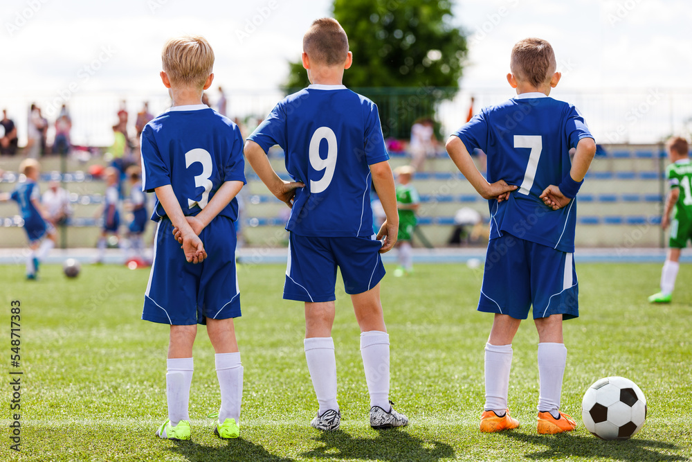 Obraz premium Football soccer match for children. Kids waiting on a pitch sideline. Sporty boys in soccer jersey clothes and cleats