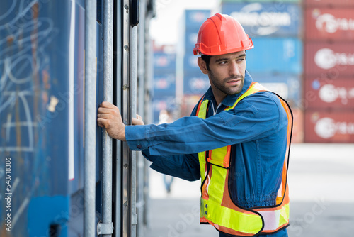 Male container yard worker opening container boxes for checking products inventory in the container yard warehouse. Male engineer checking and maintaining container box at commercial dock site