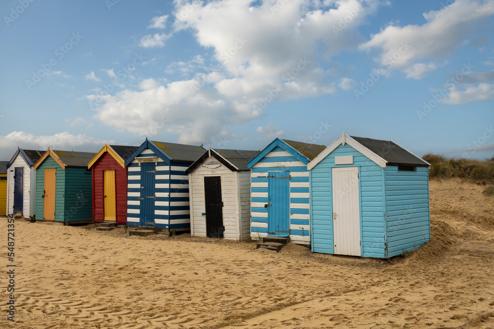 A row of colourful beach huts under a blue sky at Southwold beach in England