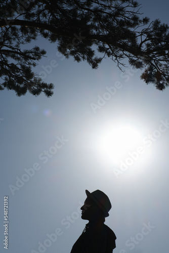 Female silhouette in profile against the sky and scorching sun. Portrait of woman in a hat.