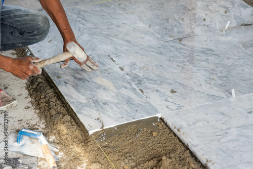 Tiler installing ceramic tiles on a floor.  construction workers laying tile over concrete floor using tile levelers, notched trowels and tile marble. 