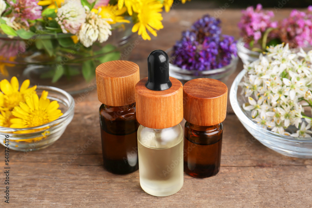 Bottles of essential oils and many beautiful flowers on wooden table Bottles of essential oils and many beautiful flowers on wooden table