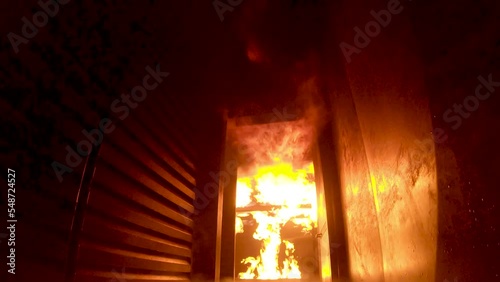 Flames erupt inside a fire training simulator and flashover along the ceiling. POV from firefighter looking up at flame and back down to level. Tilt up, tilt down.