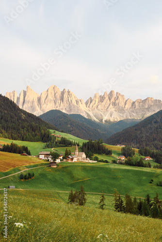 Stunning view of the Funes Valley (Val di Funes) with the Santa Maddalena Church and the mountain range of the Puez Odle Nature Park in the distance during a beautiful sunset...