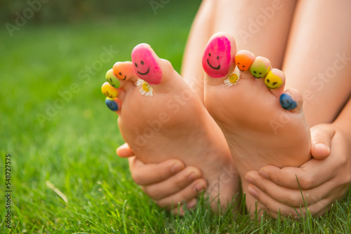 Teenage girl with chamomiles and smiling faces drawn on toes outdoors, closeup © New Africa