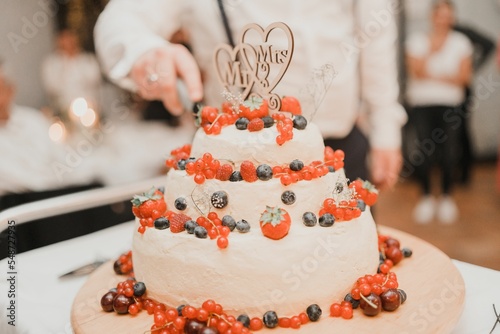 Closeup of a groom cutting a wedding cake decorated with fresh berries