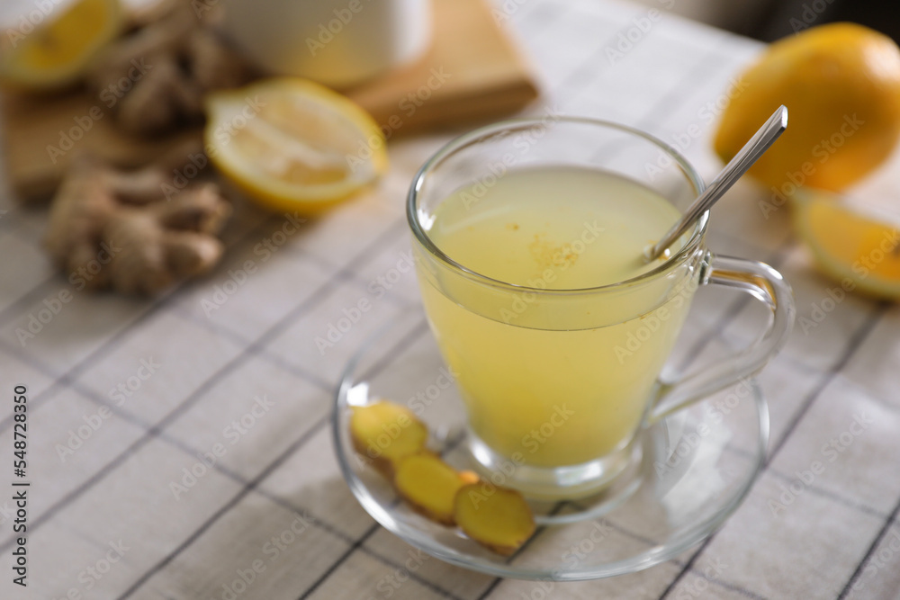 Glass of aromatic ginger tea and ingredients on white checkered tablecloth, closeup. Space for text Glass of aromatic ginger tea and ingredients on white checkered tablecloth, closeup. Space for text