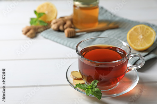 Cup of delicious ginger tea and ingredients on white wooden table, space for text