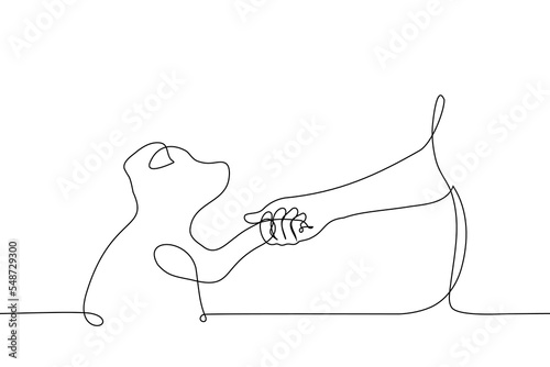 human hand holding paw of puppy looking at human - one line drawing vector. concept love for animals, a dog lover gets acquainted with a pet