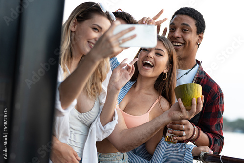 Group of multiracial friends on river boat enjoying in summer party, drinking cocktails and taking selfies © Panorama