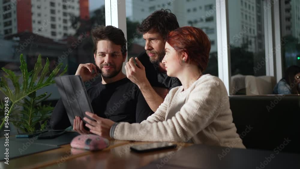 People discussing online content holding tablet seated at cafe restaurant. Group of three millennials using modern technological device People discussing online content holding tablet seated at cafe restaurant. Group of three millennials using modern technological device