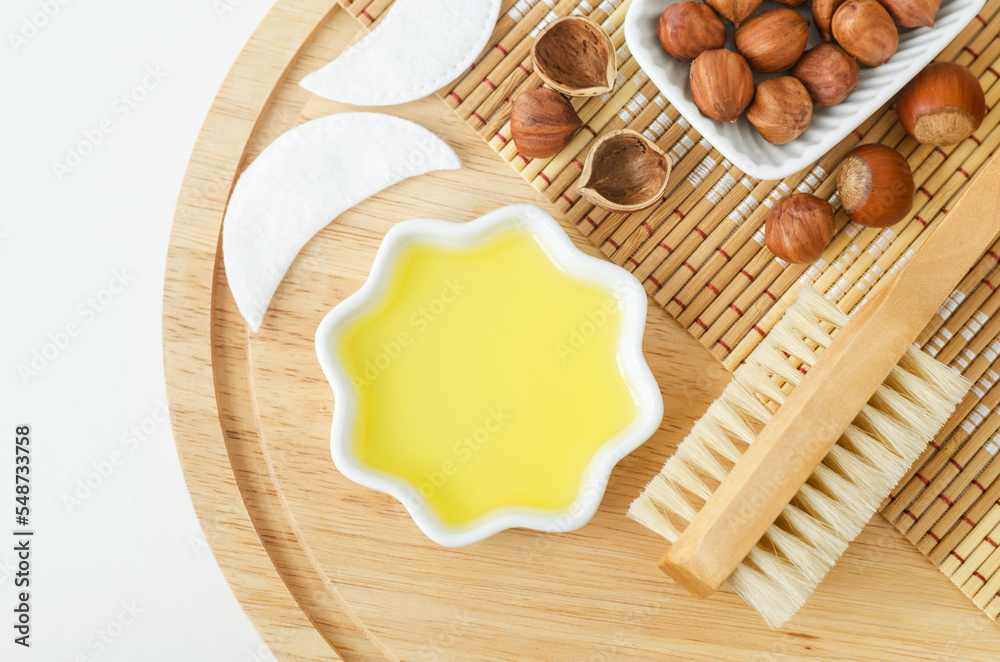 Hazelnut oil in a small white bowl and massage body brush. Natural beauty treatment and spa recipe. Top view, copy space. Hazelnut oil in a small white bowl and massage body brush. Natural beauty treatment and spa recipe. Top view, copy space.