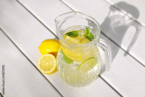 Jug of water with lemons and mint on white wooden table, above view