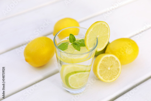 Glass of water with lemons and mint on white wooden table