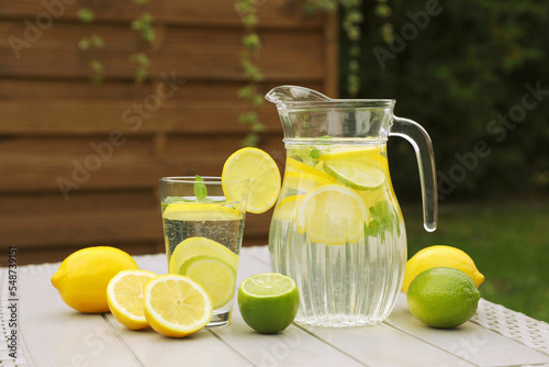 Water with lemons and limes on white wooden table outdoors