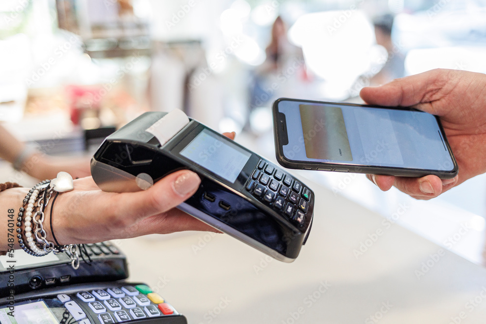 Dettaglio del pagamento con carta di credito con uno smartphone verso il pos di tenuto dalla mano di una commessa  - obrazy, fototapety, plakaty 