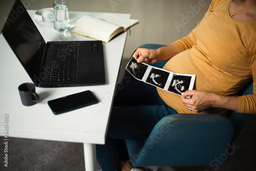 Beautiful young pregnant woman looking at ultrasound pictures of her baby. Businesswoman in office © JustLife
