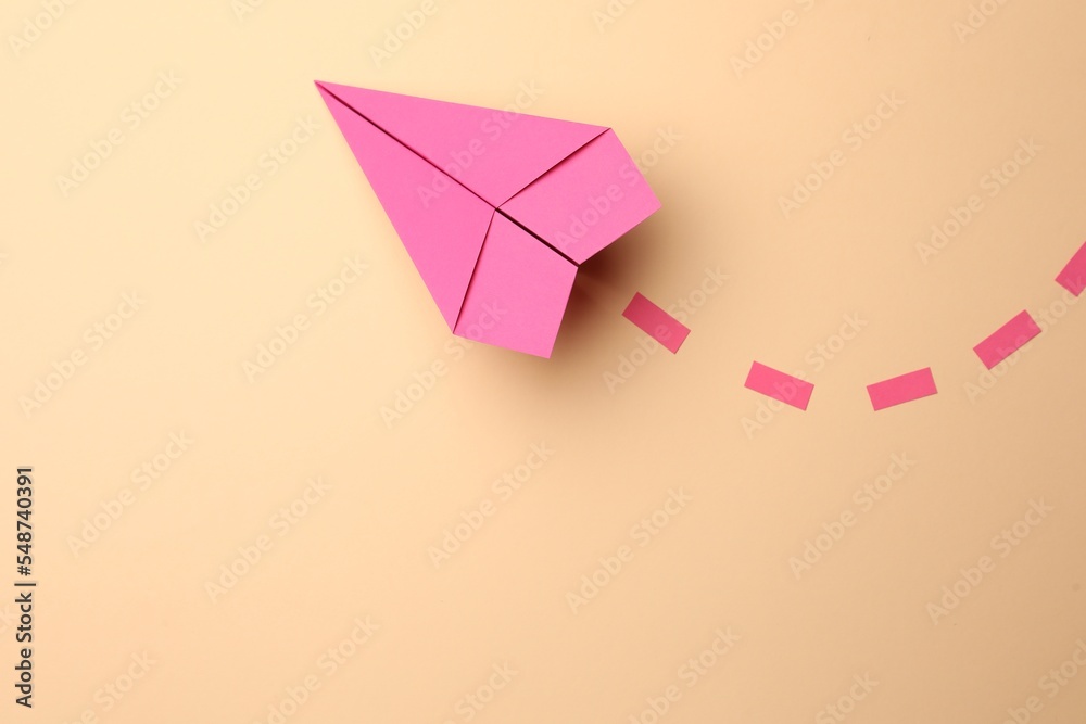 Handmade pink paper plane with dotted lines on beige background, top view. Space for text Handmade pink paper plane with dotted lines on beige background, top view. Space for text