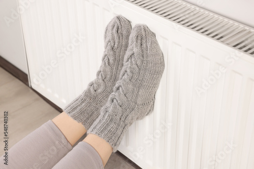 Woman warming feet near heating radiator indoors, closeup