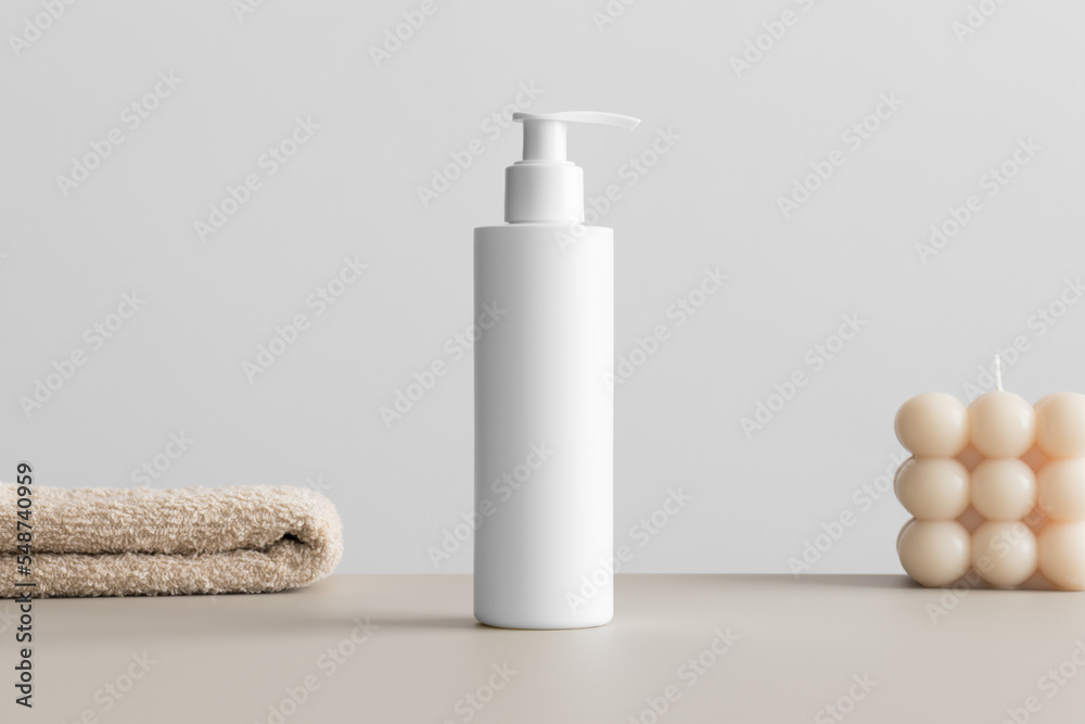 White cosmetic shampoo dispenser bottle mockup with a candle and a towel on the beige table. White cosmetic shampoo dispenser bottle mockup with a candle and a towel on the beige table.