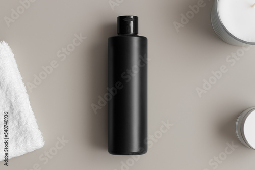 Black cosmetic lotion bottle mockup with a towel on the beige table.