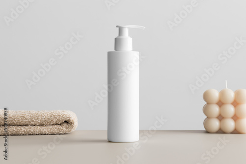 White cosmetic shampoo dispenser bottle mockup with a candle and a towel on the beige table. © Snoflinga