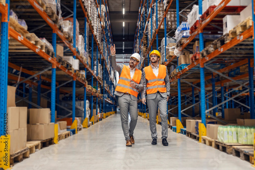 A business owner touring his business partner through storage and pointing at goods.