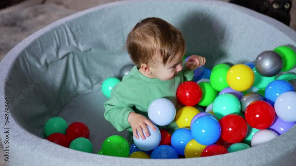 Sweet little kid sitting in the round basin waiting for the colorful balls. Somebody fills the basin with toys and the kid is rejoicing. Sweet little kid sitting in the round basin waiting for the colorful balls. Somebody fills the basin with toys and the kid is rejoicing.