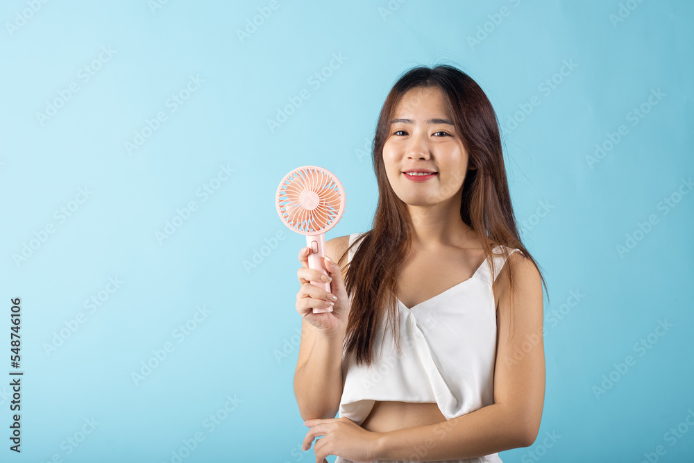 Asian beauty young woman holding pink portable electric mini fan near her face studio shot isolated on blue background, Female hand hold small plastic fan handheld she enjoying cool wind blowing Asian beauty young woman holding pink portable electric mini fan near her face studio shot isolated on blue background, Female hand hold small plastic fan handheld she enjoying cool wind blowing
