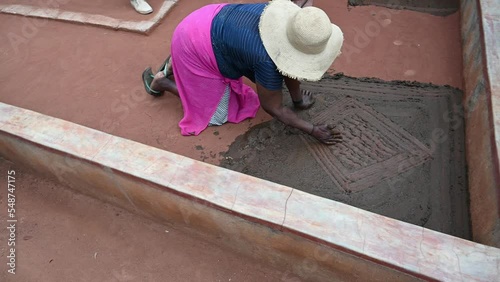 African woman creates a cow dung pattern on the front porch of her home.  An age-old folk art activity photo