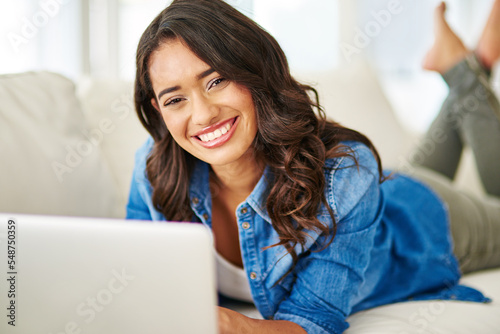 Woman, laptop and relax with smile on sofa for studying, streaming or freelance designer in remote work at home. Portrait of happy female freelancer or student smiling in comfort on living room couch