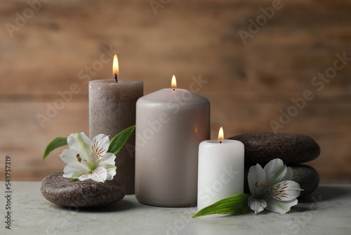 Beautiful composition with burning candles, spa stones and flowers on light grey table