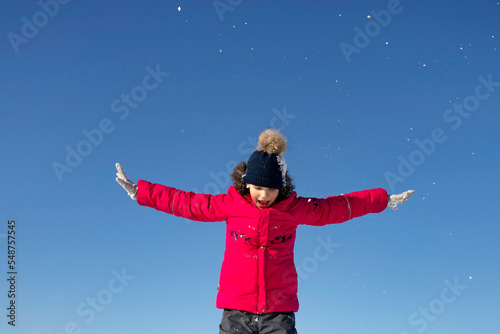 A happy child rejoices in the first snow and jumps for joy against the blue sky.