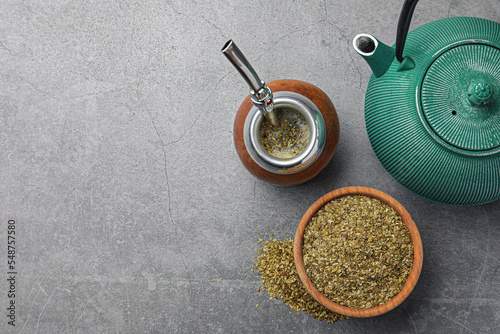 Calabash with bombilla, teapot and bowl of mate tea leaves on grey table, flat lay. Space for text