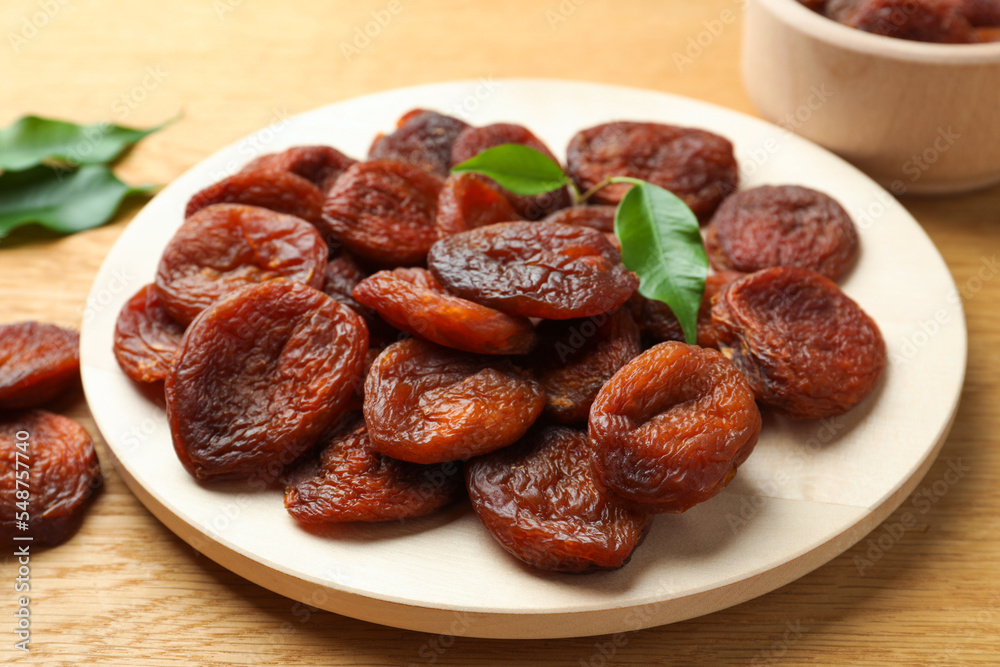 Plate of tasty apricots and green leaves on wooden table. Dried fruits Plate of tasty apricots and green leaves on wooden table. Dried fruits