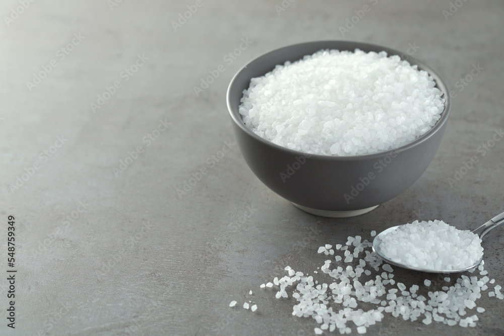 Bowl and spoon with natural sea salt on grey table, space for text Bowl and spoon with natural sea salt on grey table, space for text
