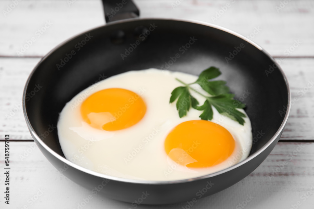 Tasty fried eggs with parsley in pan on white wooden table, closeup Tasty fried eggs with parsley in pan on white wooden table, closeup