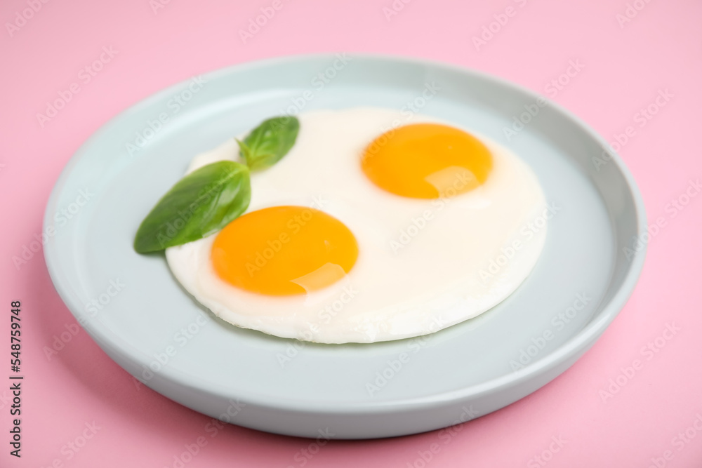 Tasty fried eggs with basil in plate on pink background, closeup Tasty fried eggs with basil in plate on pink background, closeup