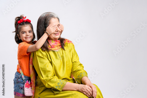 Indian little girl child closing eyes of her grandmother on white background