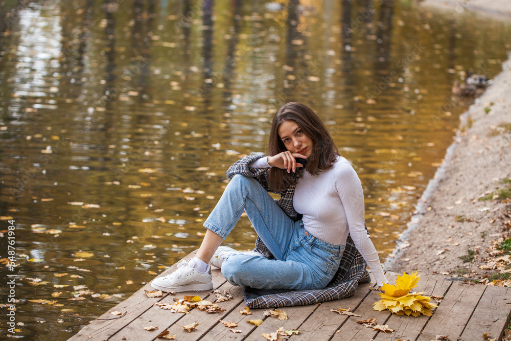 Young brunette girl in blue jeans posing in an autumn park Young brunette girl in blue jeans posing in an autumn park