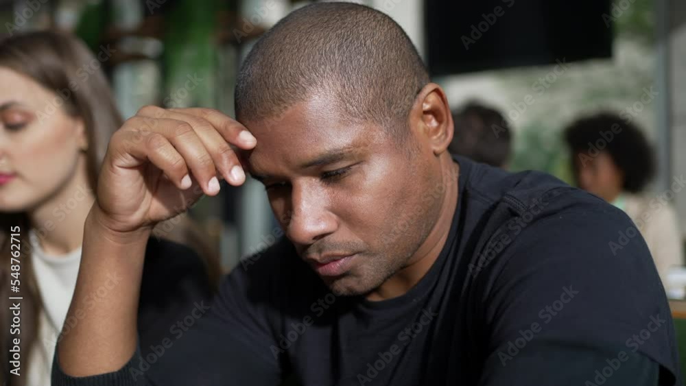 A worried black man feeling anxious seated at coffee shop restaurant. Preoccupied African American person with worried emotion A worried black man feeling anxious seated at coffee shop restaurant. Preoccupied African American person with worried emotion