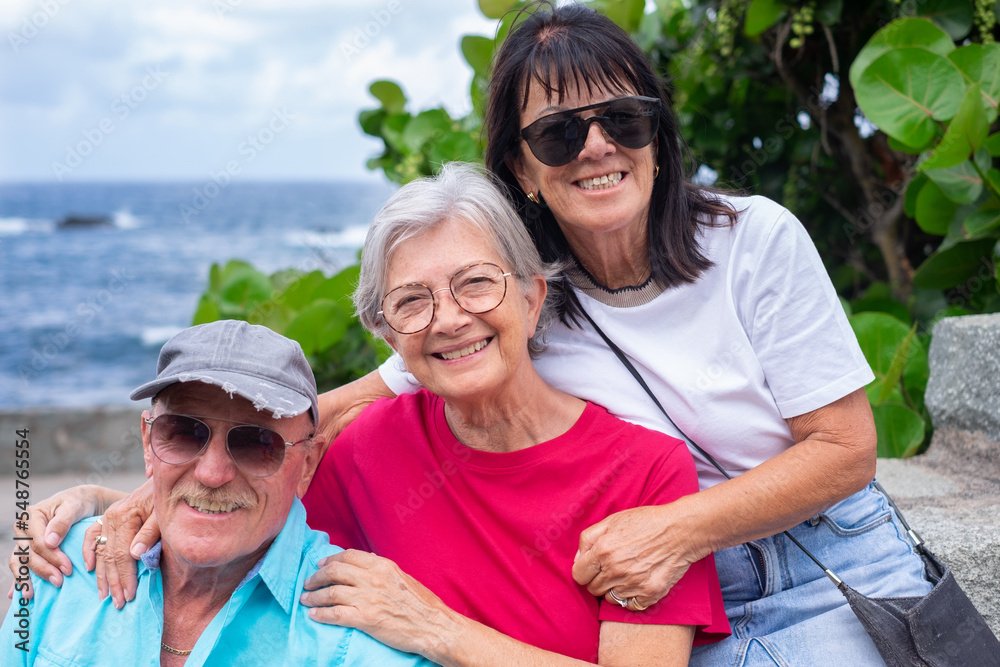 Group of beautiful caucasian friends sitting at the beach enjoying the day outdoors looking at camera smiling. Seniors people enjoying retirement, free time and vacation