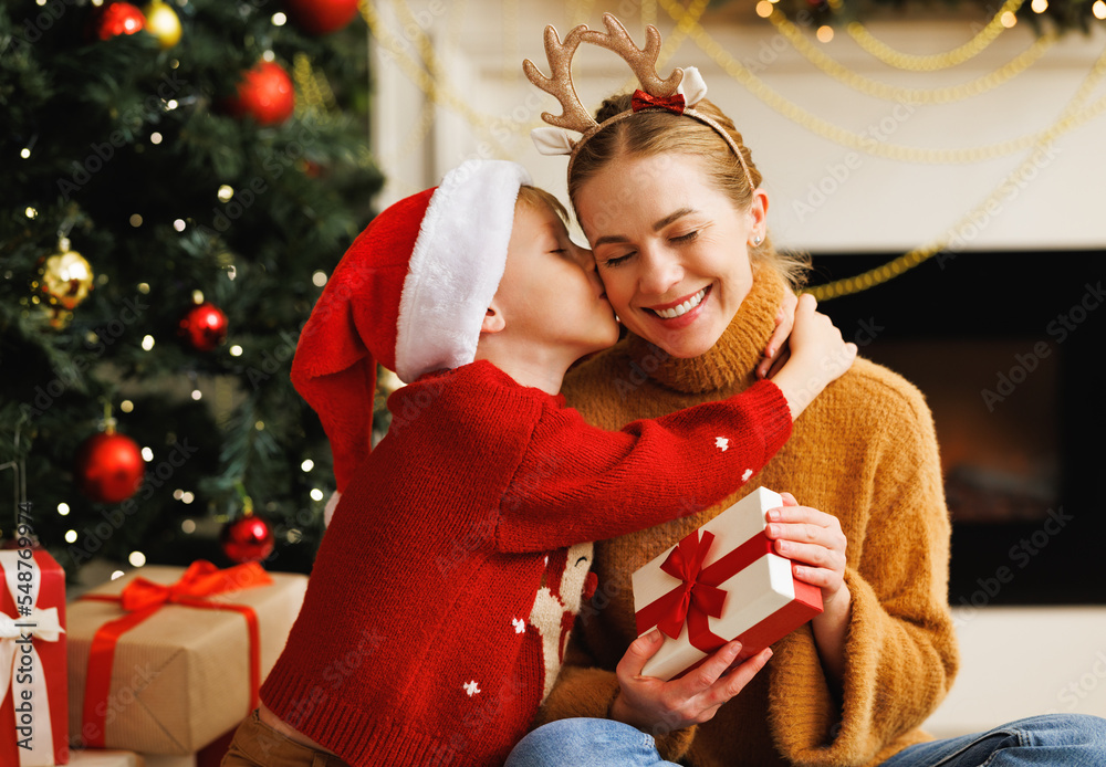 Cute child smiling embracing and kissing mother opening christmas ...