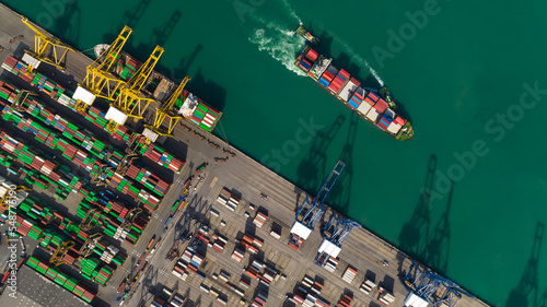 commercial port loading and unloading cargo from container ship import and export by crane for distributing goods by trailers transported to customers and dealers, aerial view