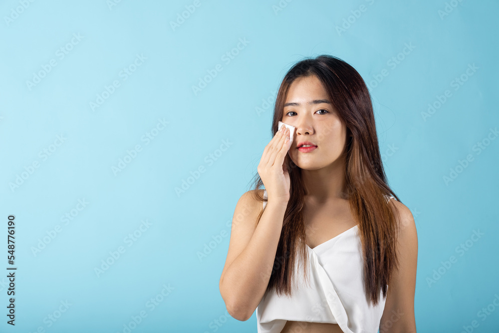 Facial Beauty Treatment. Asian beautiful young woman removing cosmetic make up using pad cotton face cleaner disc, studio shot isolated on blue background, Portrait of happy female cleaning face Facial Beauty Treatment. Asian beautiful young woman removing cosmetic make up using pad cotton face cleaner disc, studio shot isolated on blue background, Portrait of happy female cleaning face