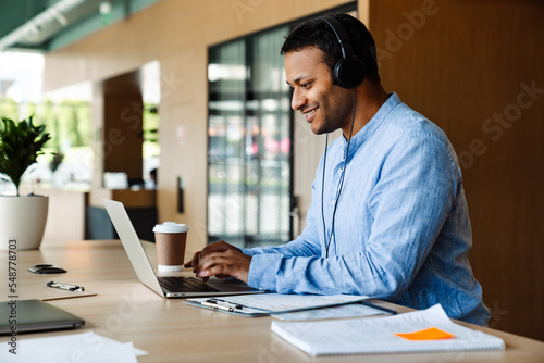 Indian businessman in headphones working on laptop computer in office
