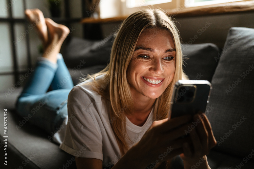 Blonde white woman using mobile phone while resting on couch Blonde white woman using mobile phone while resting on couch
