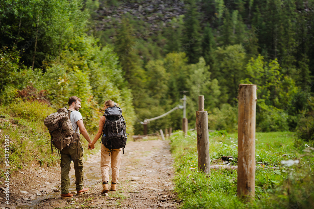 White young couple with backpacks hiking in green forest White young couple with backpacks hiking in green forest