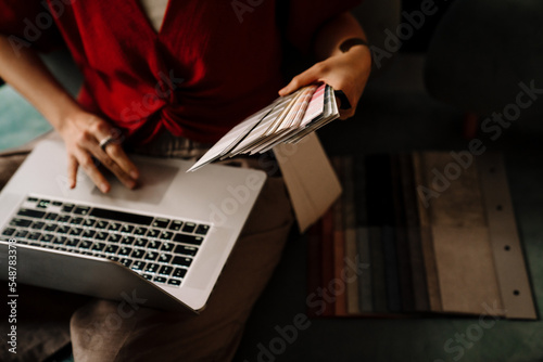 Close up hands of woman interior designer sitting on sofa while holding catalogue of colors and laptop